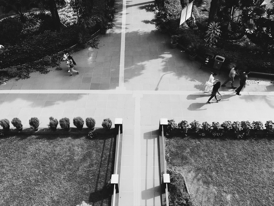 People and long shadows crossing a geometric courtyard